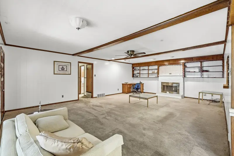 Living room with exposed wood ceiling beams, a brick wood-burning fireplace and built-in shelving