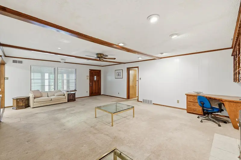 Living area by the wood front door with a built-in desk and windows with blinds