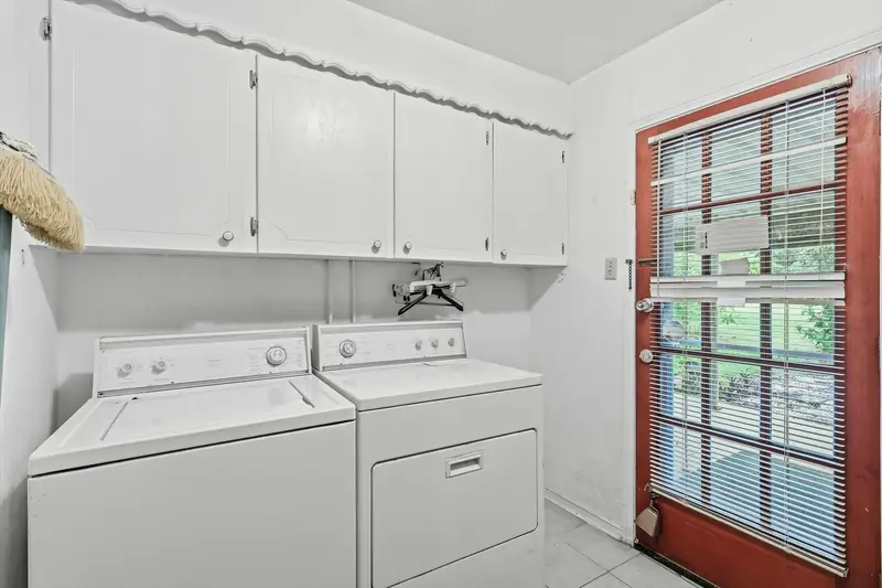Laundry room with washer and dryer, white upper cabinets and a red exterior door
