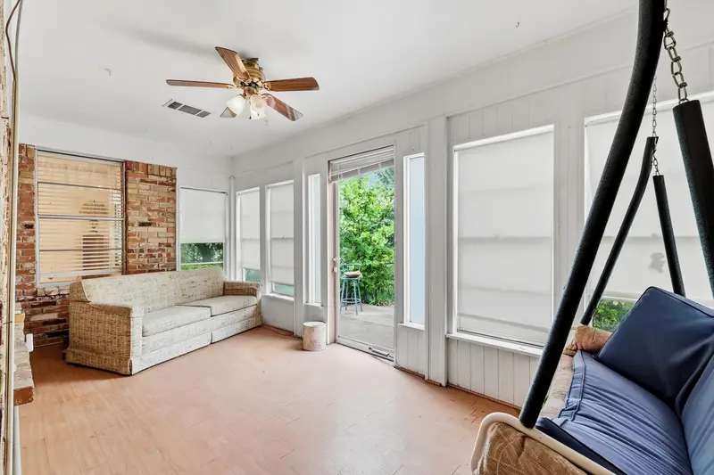 Sunroom with a wood-look floor, exposed brick accent wall, a wall of windows and a hanging porch swing