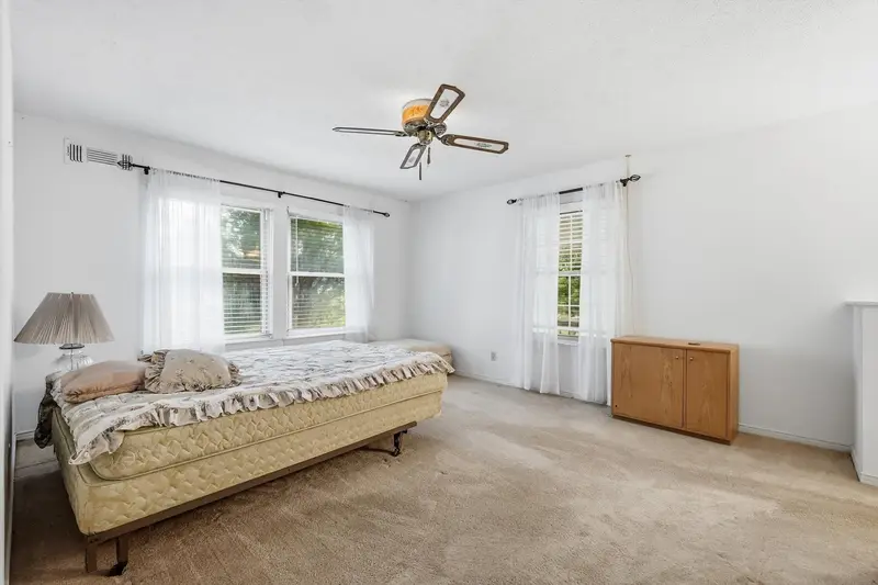Primary bedroom with two curtained windows and a ceiling fan