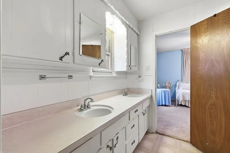 Bathroom with double sinks, mirrored cabinets and tile floor, opening to a bedroom
