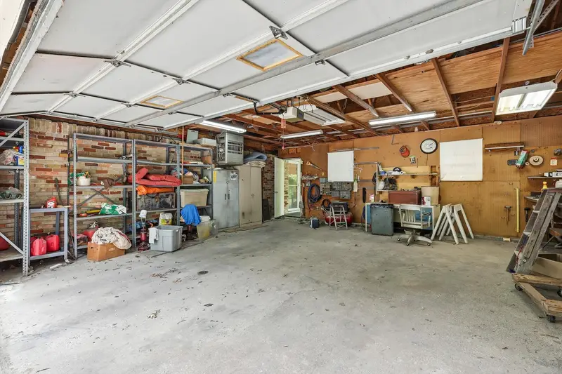 Detached garage interior with concrete floor, exposed rafters, metal shelving and a workbench
