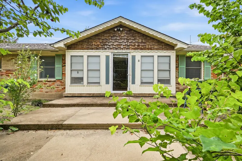 Front entry with a cedar-shingle gable over a glass storm door, brick and siding facade and green shutters