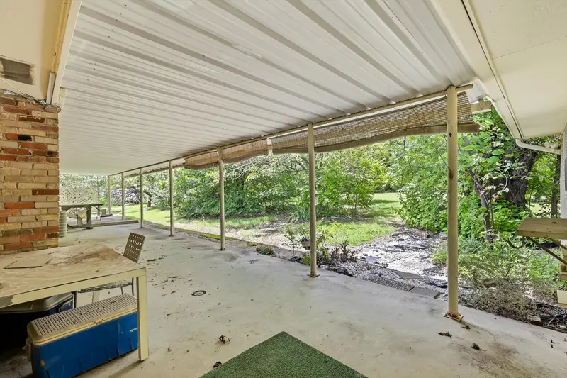 Long covered back patio under a white metal awning with the brick chimney and backyard beyond