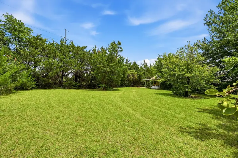 Open mowed field behind the home bordered by cedars, with a small outbuilding at the tree line