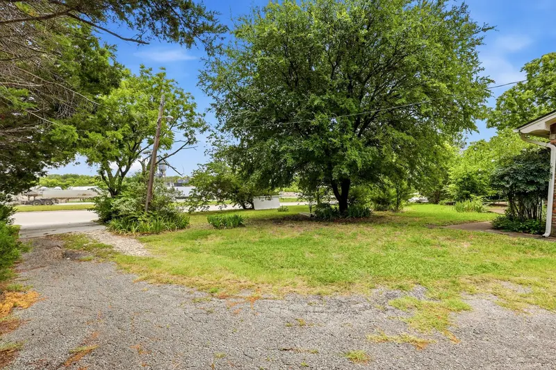 Front yard with a gravel driveway and large shade tree looking out toward State Highway 205
