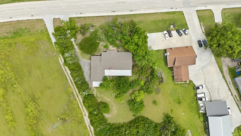 Near top-down aerial of the home centered on its treed lot with the driveway and highway at top