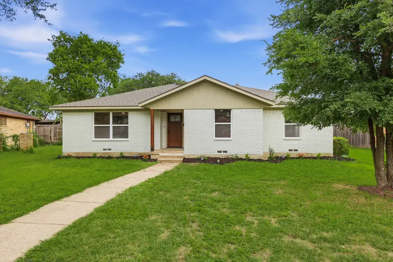 White-painted brick single-story home with a craftsman door and shade tree