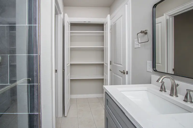 Bath with a glass walk-in shower, gray quartz-topped vanity and built-in linen shelving