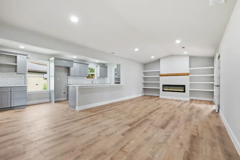 Open great room with a gray kitchen, island and fireplace under a vaulted ceiling