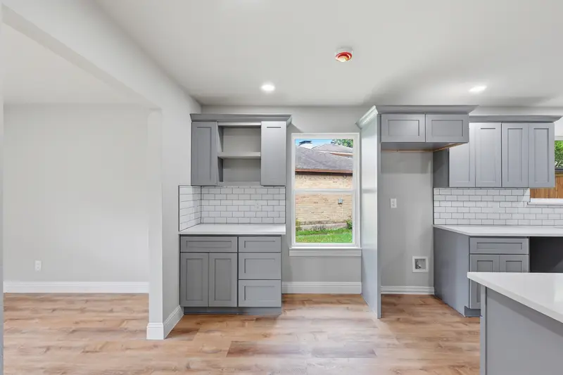 Gray shaker cabinets, open shelving and white subway tile beside a bright window