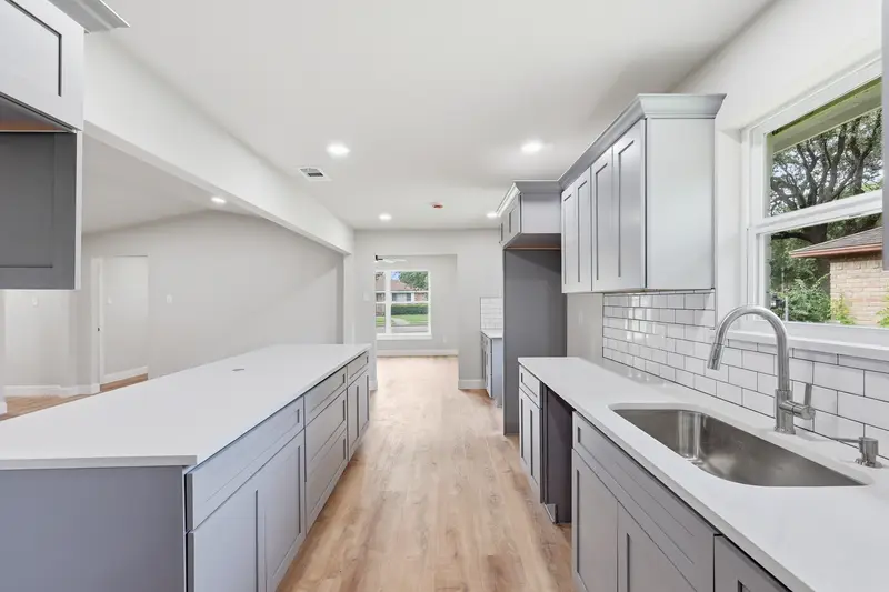 Kitchen island in white quartz with a stainless sink, subway tile and window