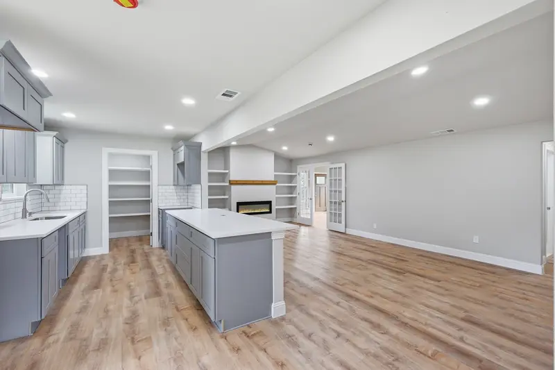 Wide open-concept view of the kitchen island, pantry, fireplace and living area