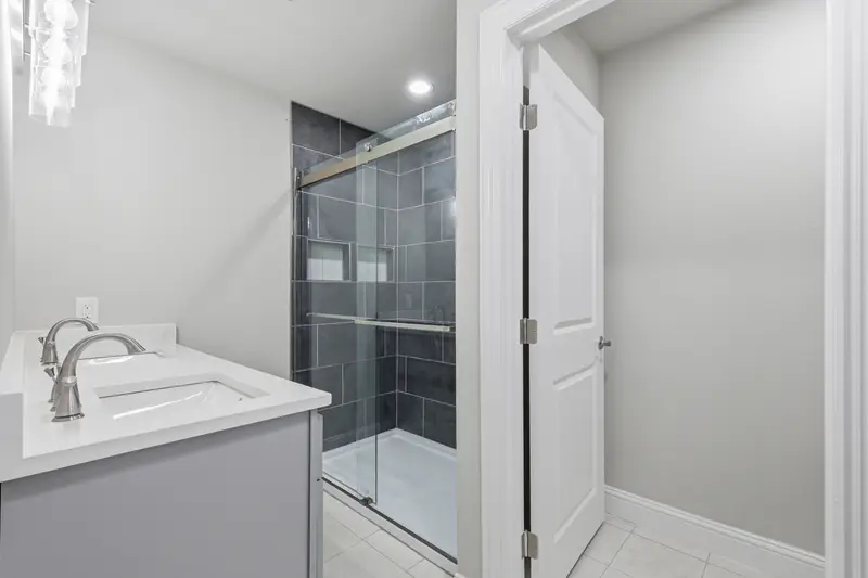 Updated bath with a gray vanity, white quartz and a glass walk-in shower with dark tile