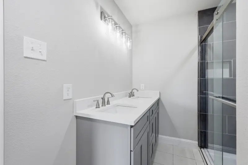 Primary bath with a double gray vanity, white quartz and a glass shower with dark tile