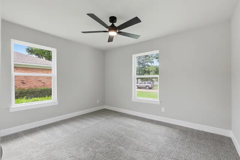 Carpeted bedroom with two windows, a ceiling fan and neutral walls