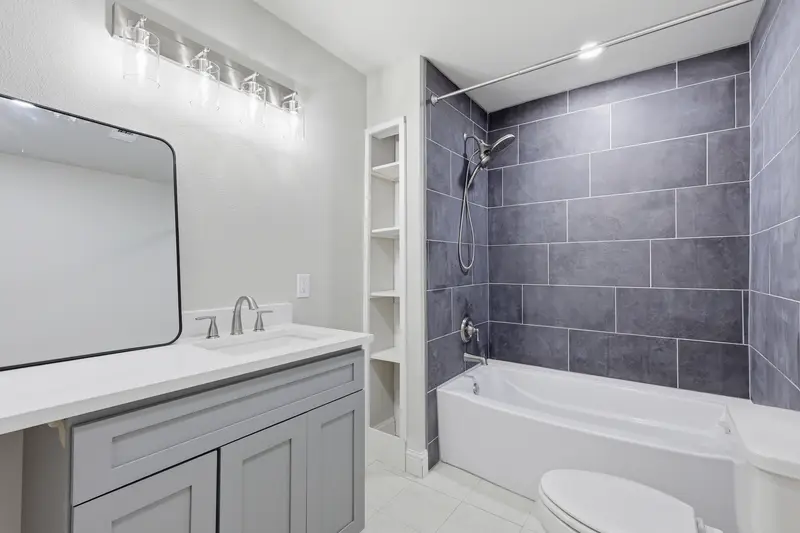 Hall bath with a new gray vanity, quartz top and a tub-shower with dark tile surround