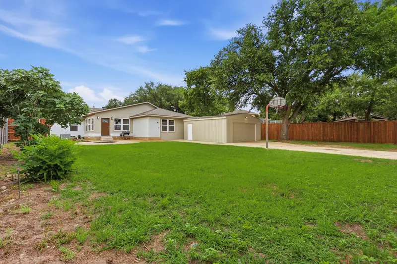 Wide backyard with the rear of the home, detached garage, big lawn and mature trees