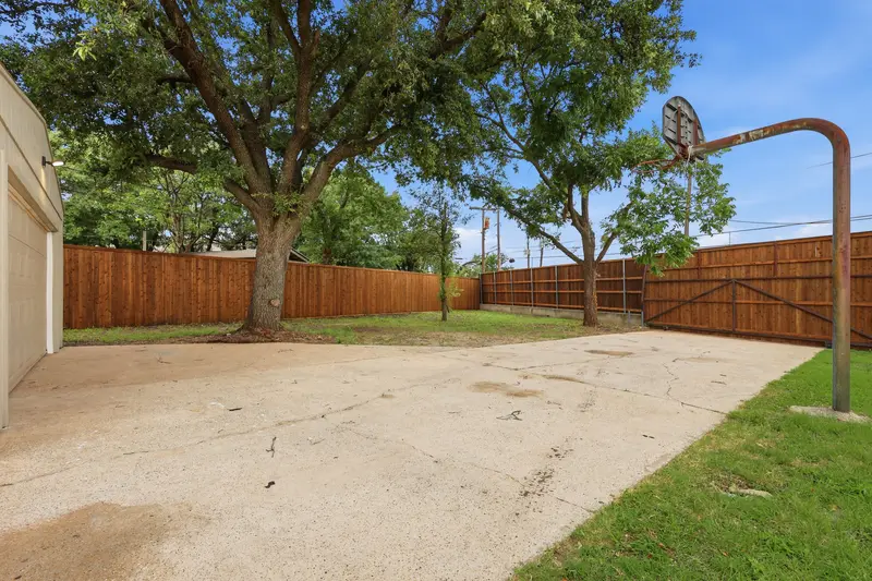 Concrete sport court with a basketball goal shaded by mature trees and cedar fence