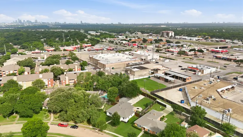 Aerial over the neighborhood with the Dallas skyline on the horizon and nearby retail